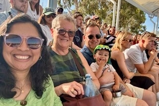 An older woman with short hair sits between a young family.