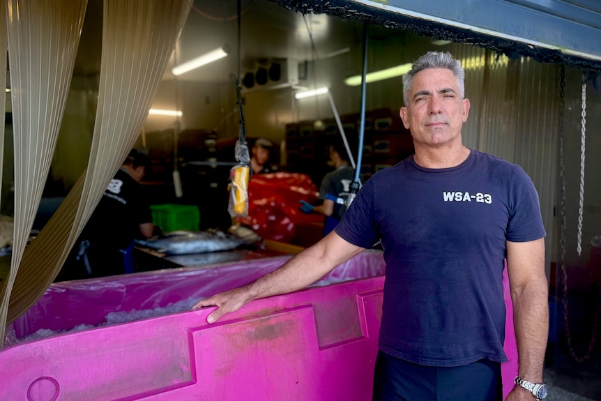 A man with grey hair wearing a blue t-shirt and standing next to a purple skip bin.