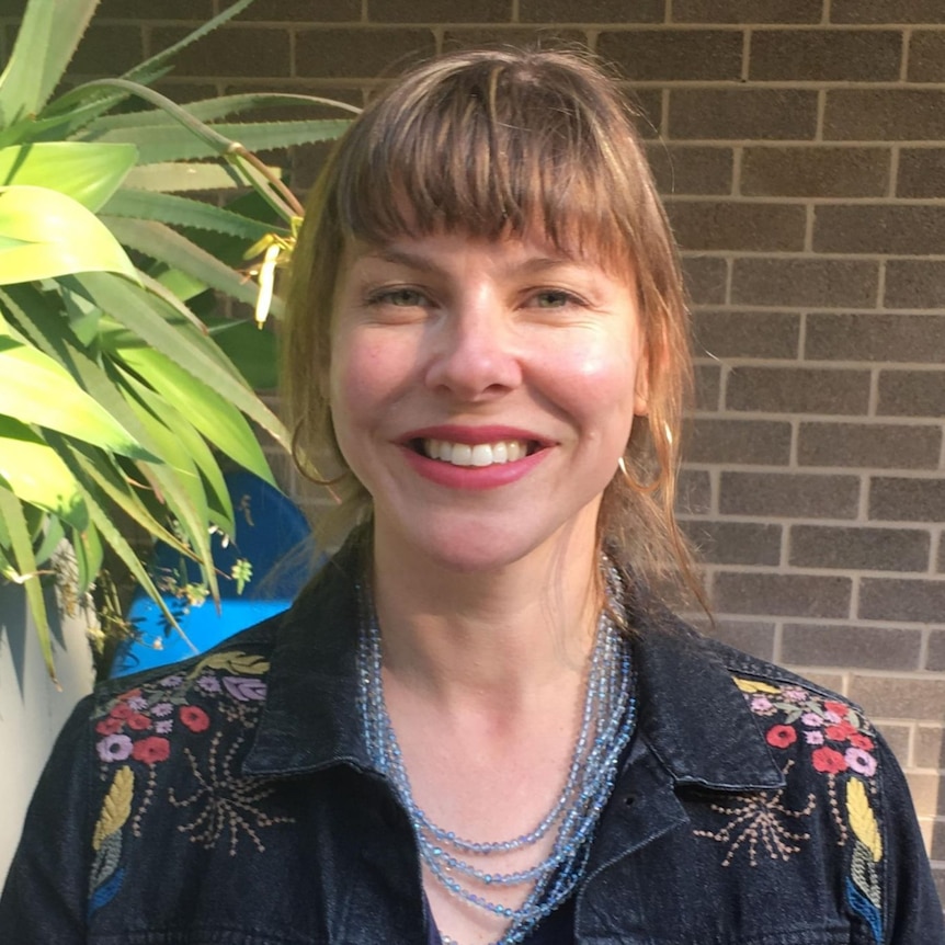 Professional CEO lawyer smiles at the camera. there is a brick wall and plant in the background. 