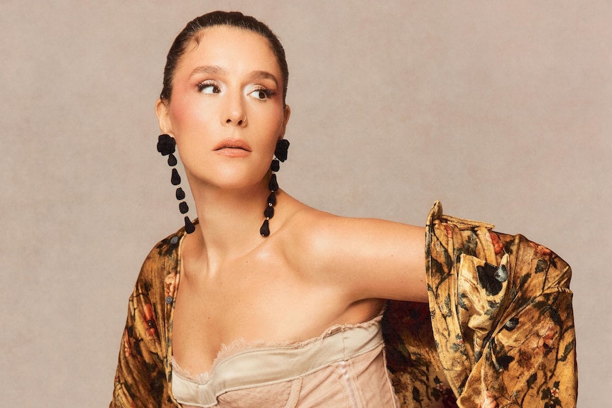 Glamorous British woman poses wearing elaborate jewellery and make-up, corset, gold flower print jacket, leopard leggings