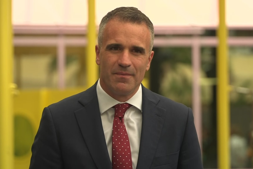 Peter Malinauskas in a business suit fronting cameras at a playground