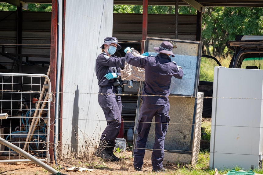 Two people wearing protective gear, gloves, and masks appearing to inspect a piece of material in a garden.