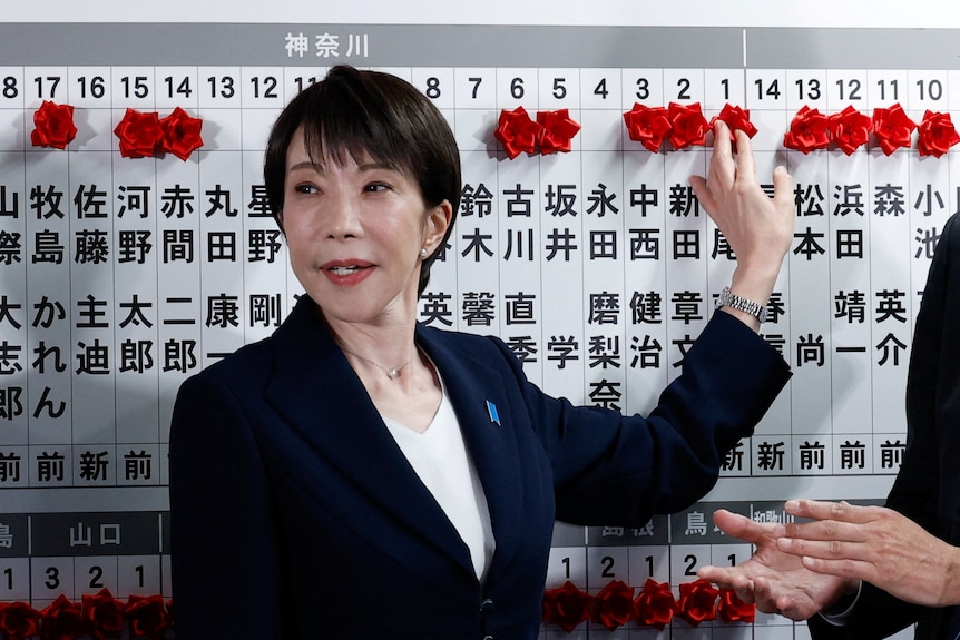 Sanae Takaichi standing in front of an election tally board.