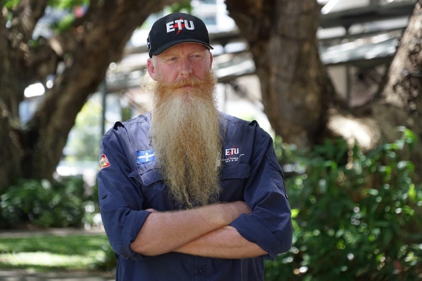 A man with his arms folded and a ETU hat looks seriously at the camera.