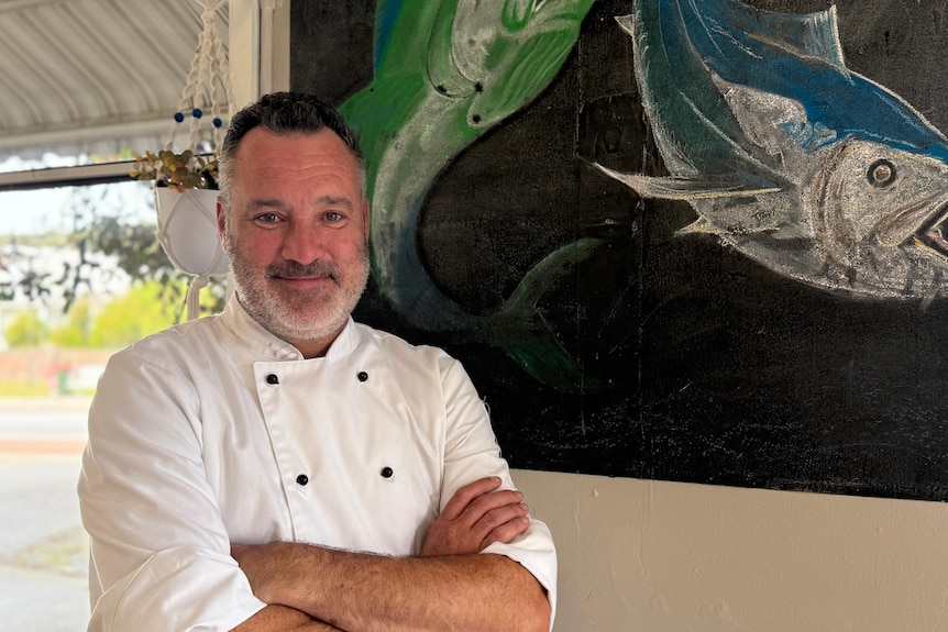 A man stands in front of a chalkboard with a fish drawn on it.
