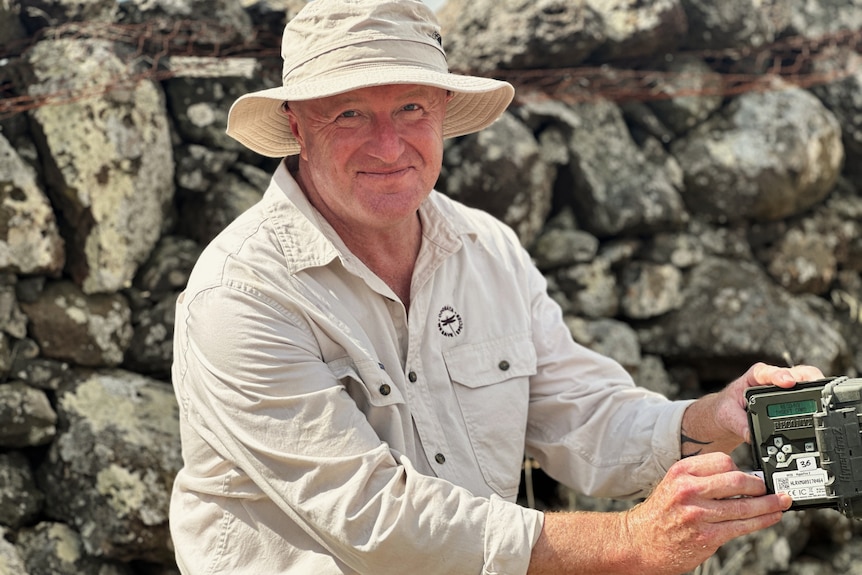 A man with rocks in the background and a camera in hand.