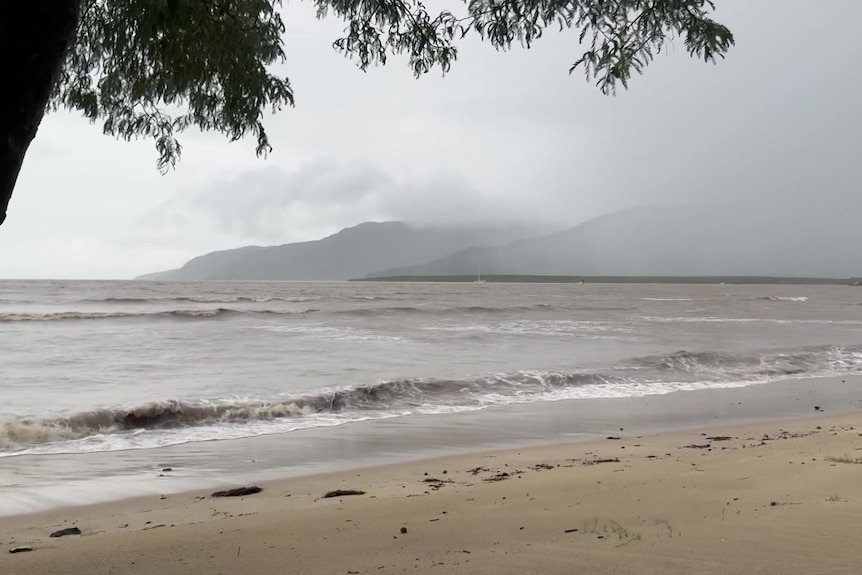 A murky tide rolls onto a deserted beach on an overcast day.