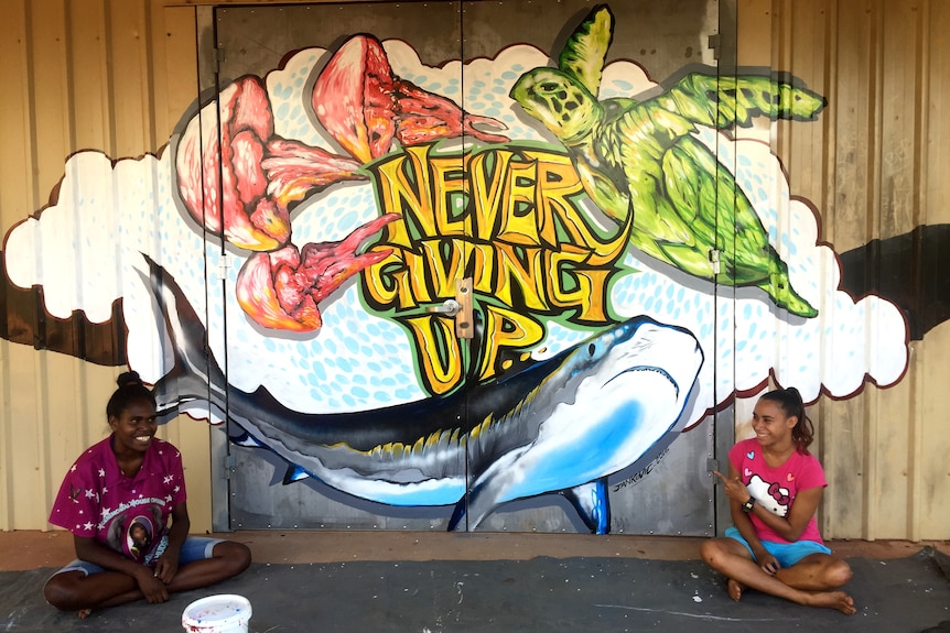 A mural saying never give up with two girls smiling next to it.