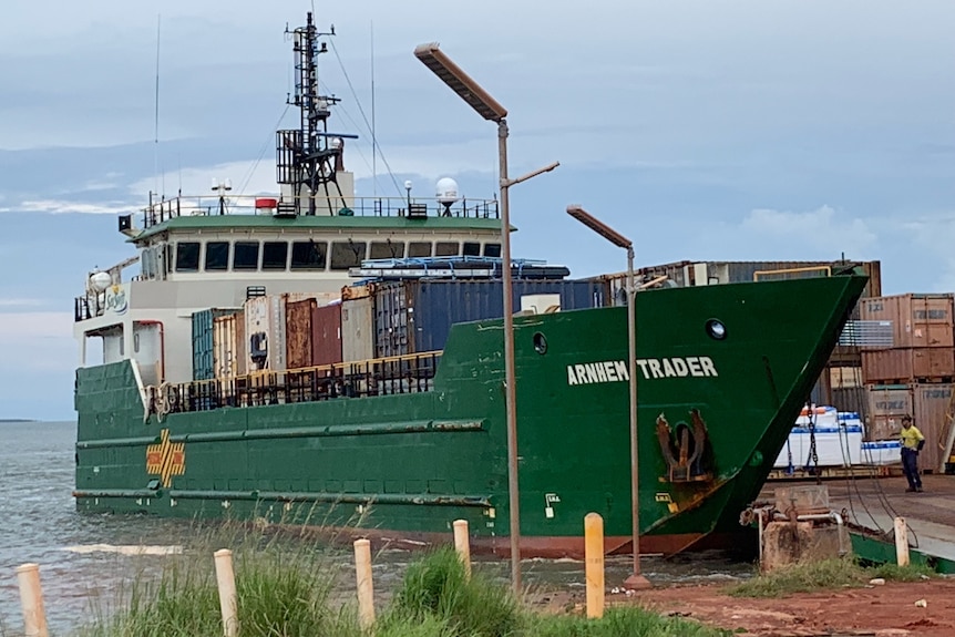 A barge, loaded with shipping containers full of stock, is docked at the ocean's edge.