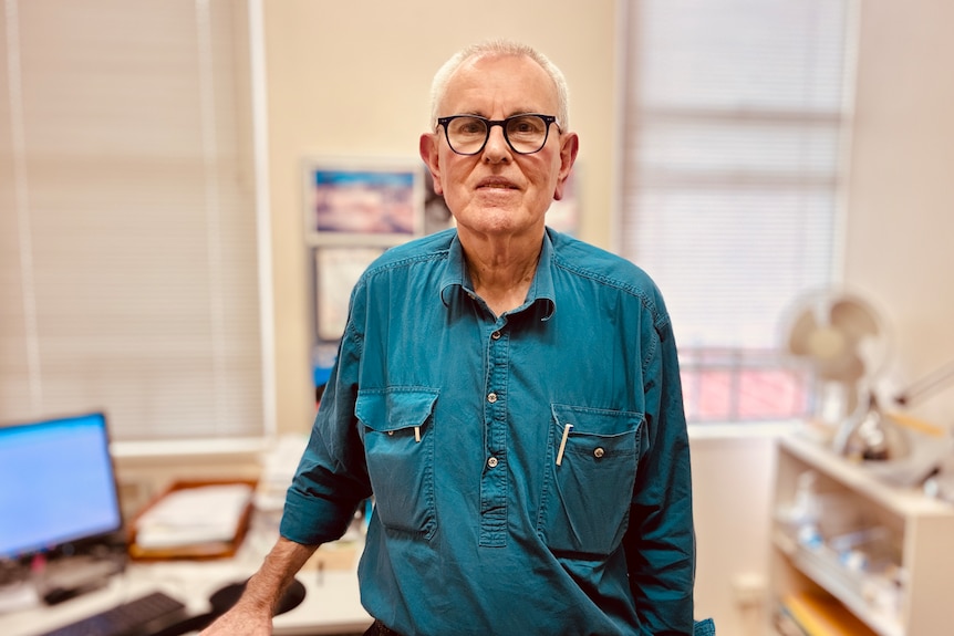 An older man in glasses stands in an office.