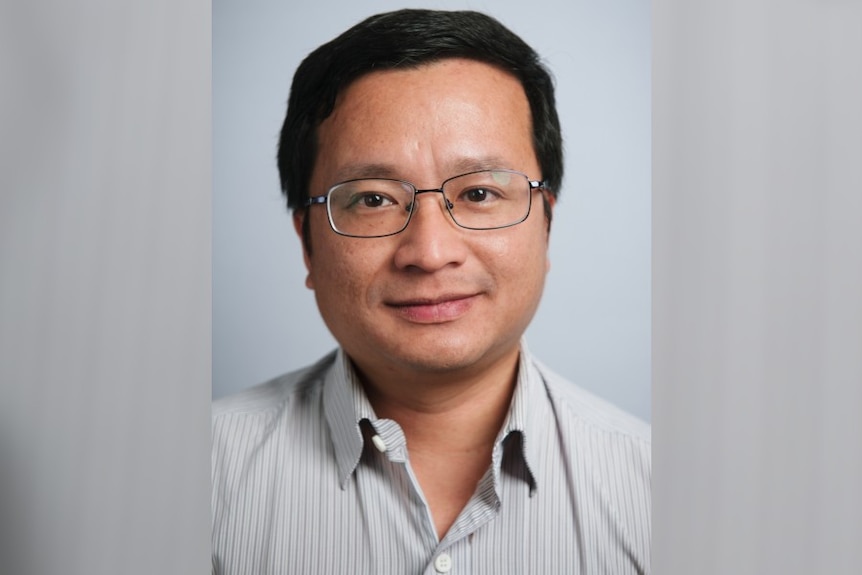 A man wearing glasses looks straight at the camera with a neutral expression.