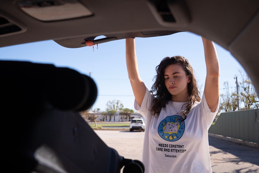 A young, dark-haired woman raises her arms to close a car boot.
