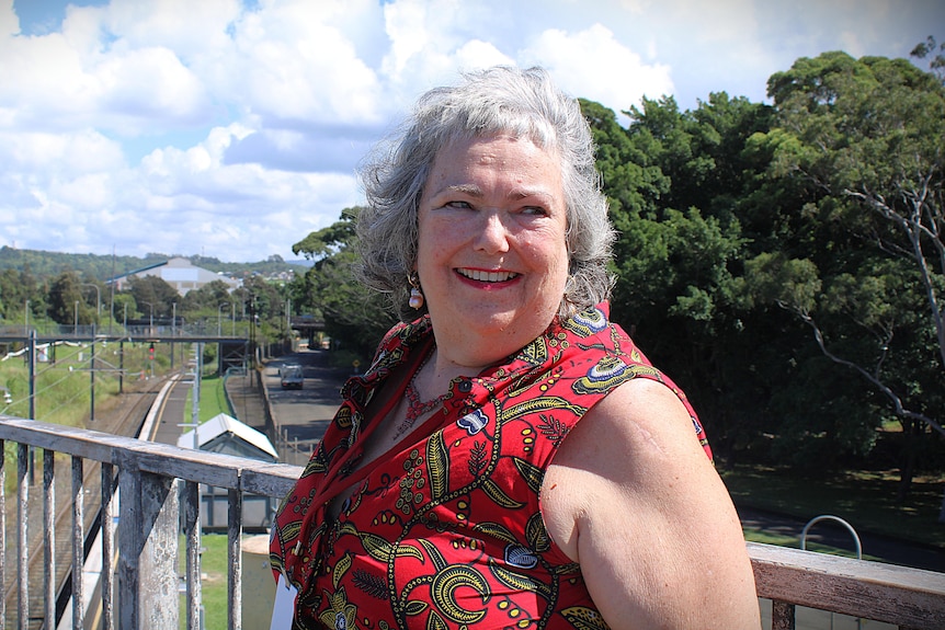 Woman with grey hair and red clothing smiling near industrial site