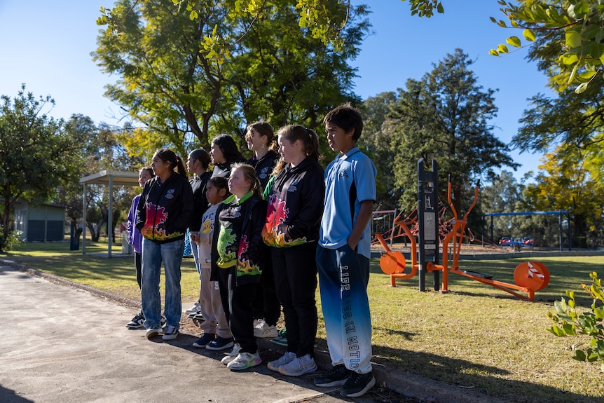 Ten young children stand on the side of the road in an orderly manner.