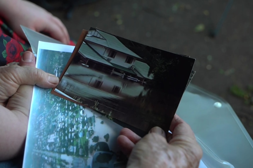 Two hands holding each other while looking at old photos of a flooded house
