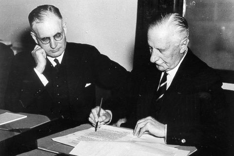 A black and white photo of two people signing a document. 