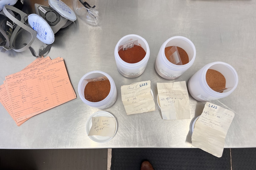 Four samples of orange soil in small containers.