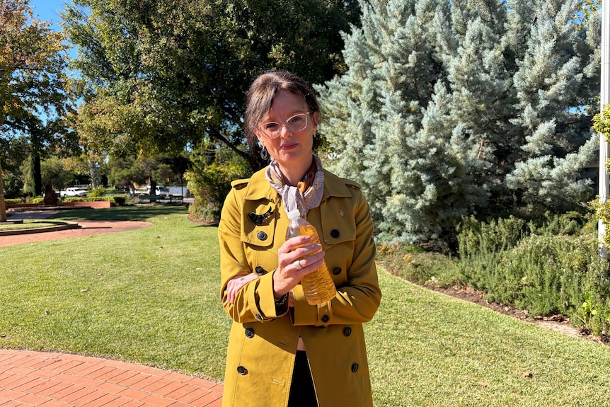 Steph is outside looking at camera holding bottle with yellow-coloured water inside.