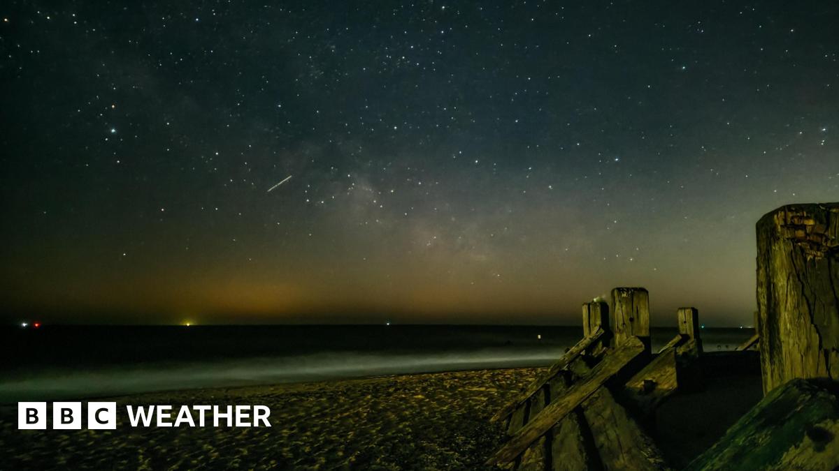 night sky image from a beach overlooking the sea.  Lots of bright white spots in the sky and one streak of light showing a meteor streak