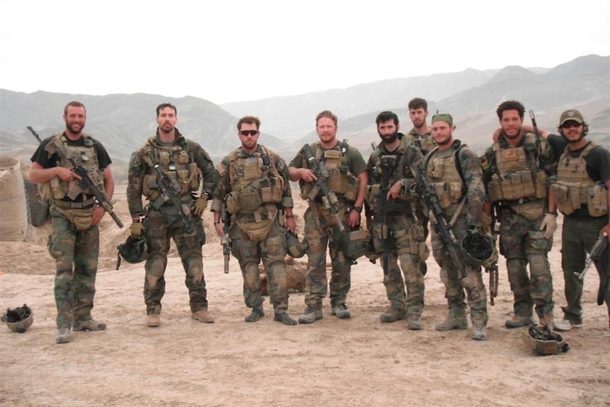Nine men in military uniforms standing in the desert. 