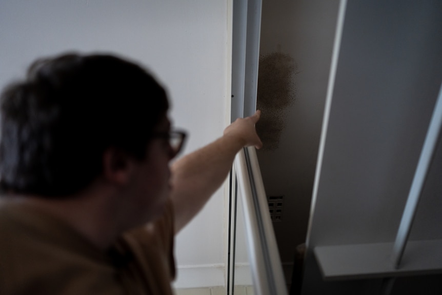 Brett points up to mould growing in the ceiling of his bedroom.