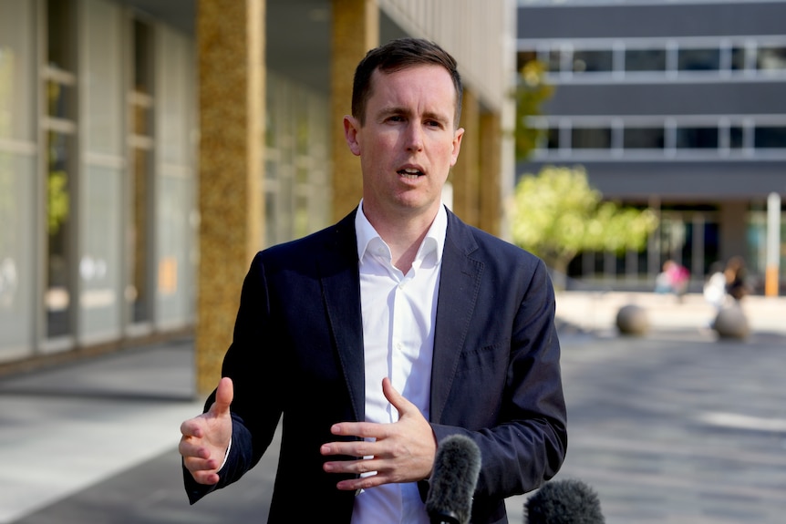 A man in a suit jacket speaks outside.