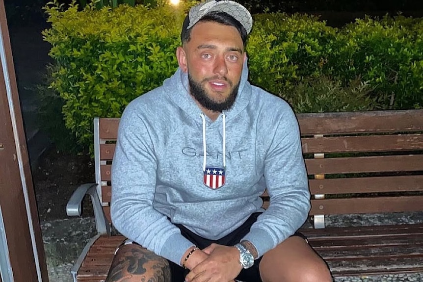 A man in a cap and sweatshirt sitting on a park bench.