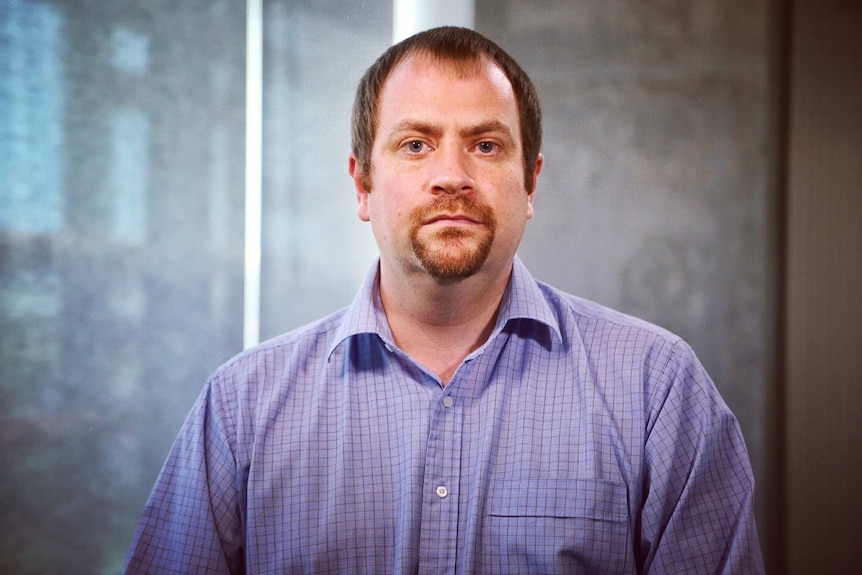 A serious-looking man in a checked shirt, looking at the camera.