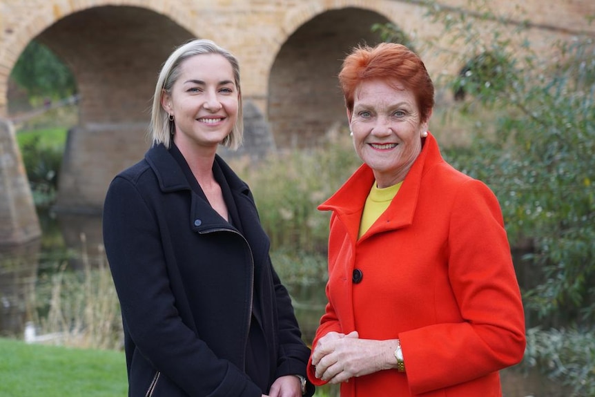 Two women stand near an old stone bridge.