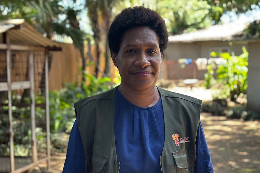A woman smiles at the camera wearing a green vest and a blue shirt
