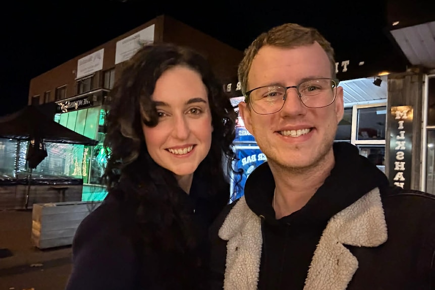 Woman and man smile in selfie at night on street.