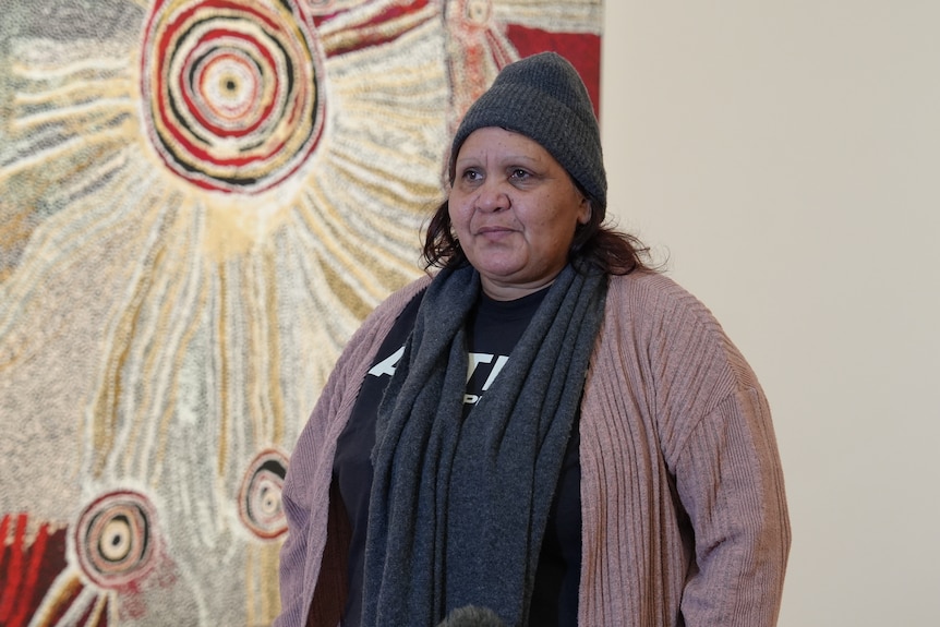 A woman smiles in front of an artwork.