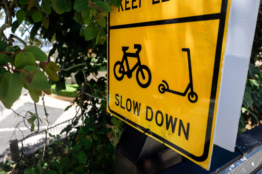 A yellow sign warning people to slow down on their bikes and e-scooters.