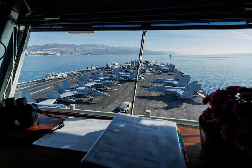 a view through the front window of a ship carrying jet planes on the deck