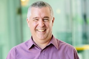 A middle-aged man in a purple dress shirt with a big smile