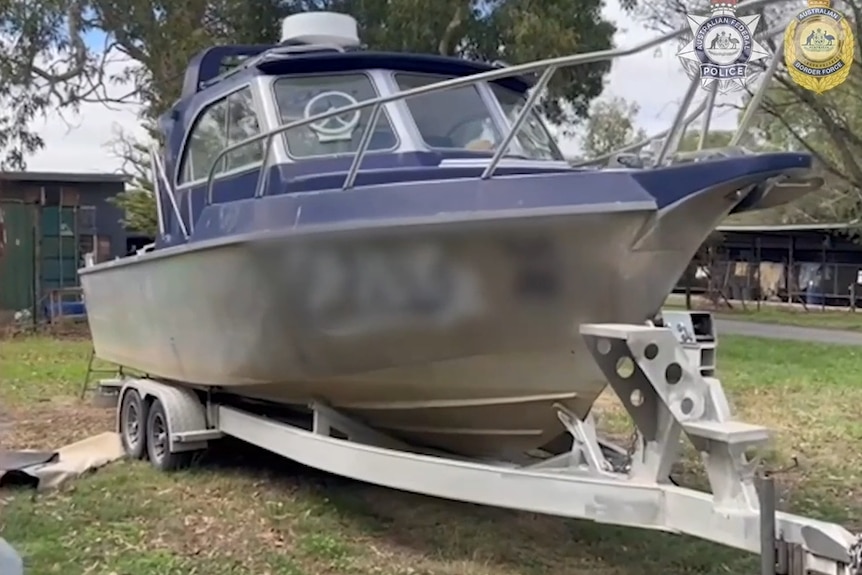 A boat on a trailer sitting on a grassed area.