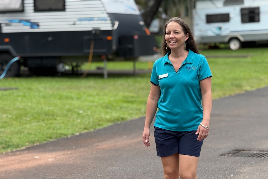 A woman wearing a teal polo walking down a road in a caravan park.