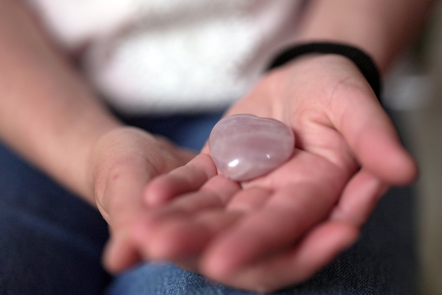 A woman's hands hold a pink heart-shaped stone