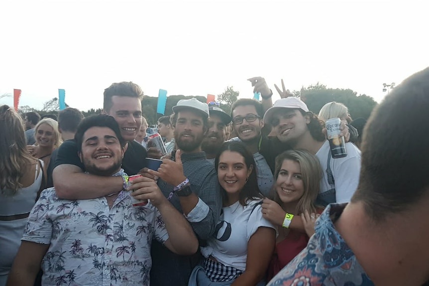 A group of young people in a festival setting smile for a photo. 
