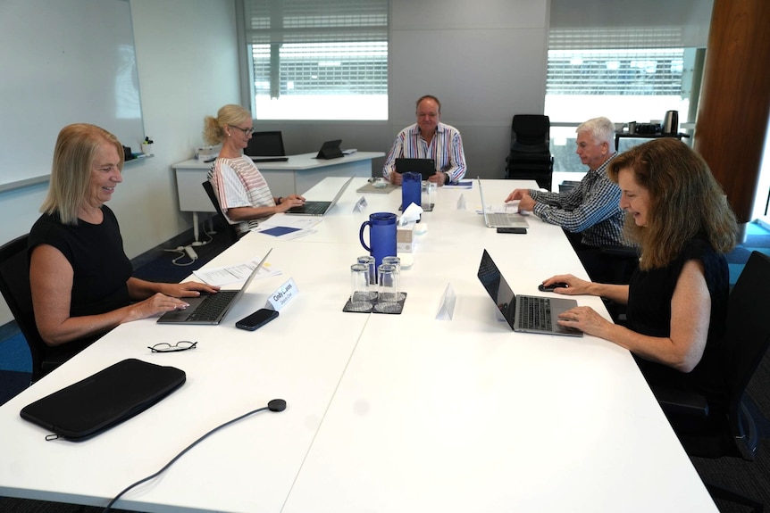 People meeting in an office, sitting around a table with their laptops.