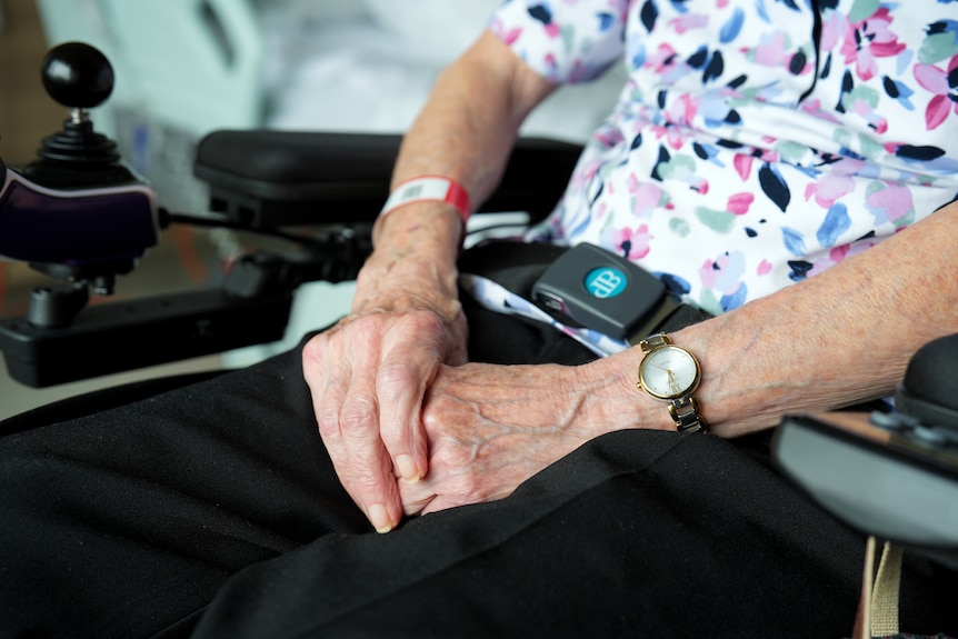 An older person's hands sitting on their lap as they sit in a motorised wheelchair.