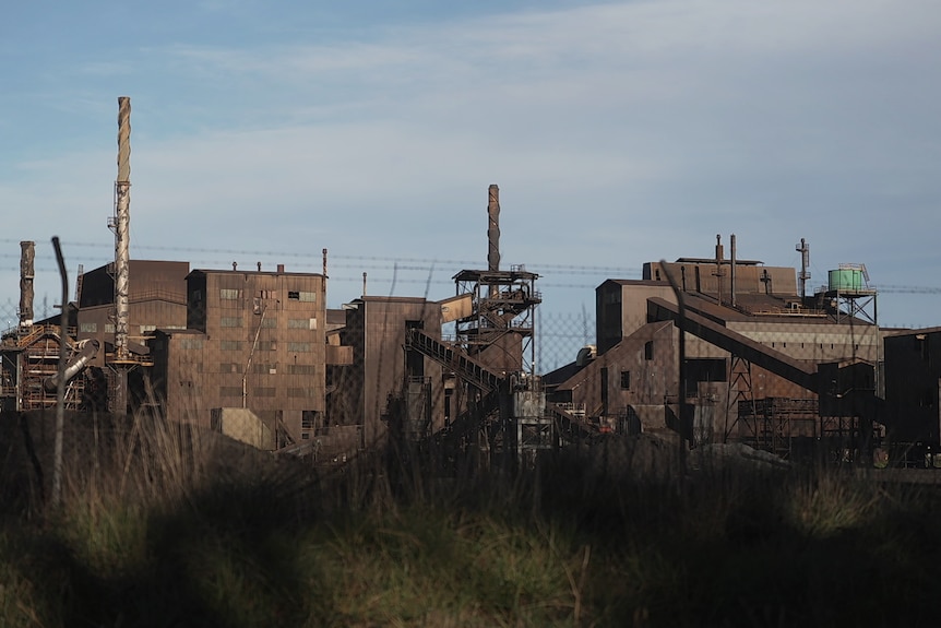 Large industrial complex featuring brick structures, smokestacks, and equipment, enclosed by a perimeter fence.