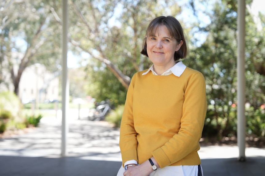 A woman with a light-coloured bob stands outdoors smiling.