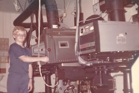 A young man standing behind a movie projector.