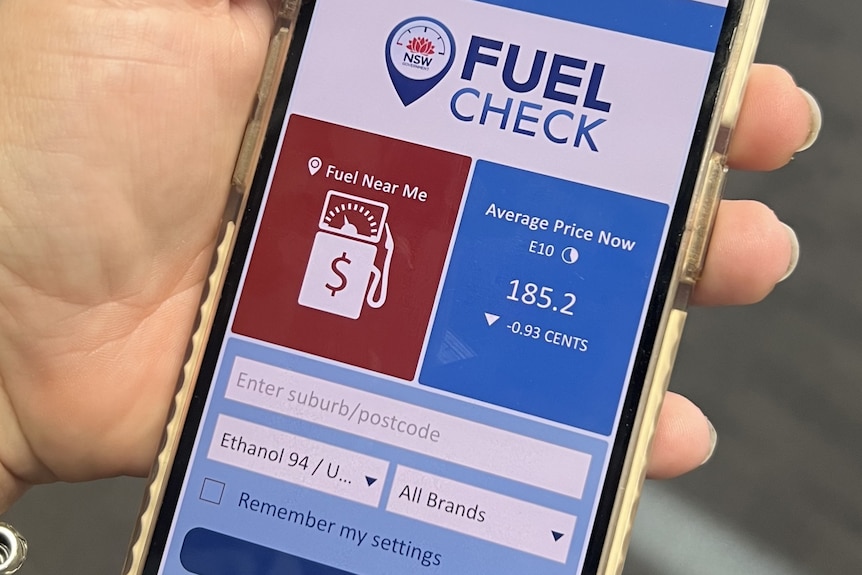 A hand holding a mobile phone with the FuelCheck app open.