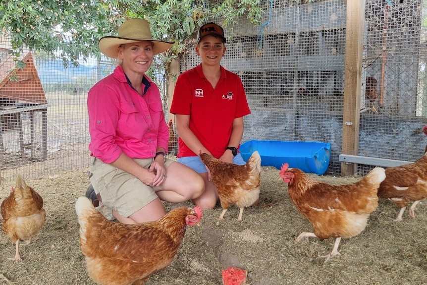 A woman in a pink shirt and a boy in a red shirt kneel down with chickens.