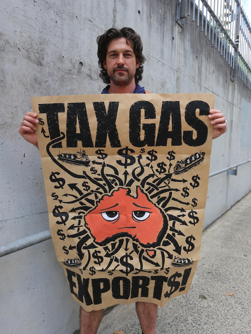 A man holds a poster with an image of Australia surrounded by dollar signs and the words tax gas exports