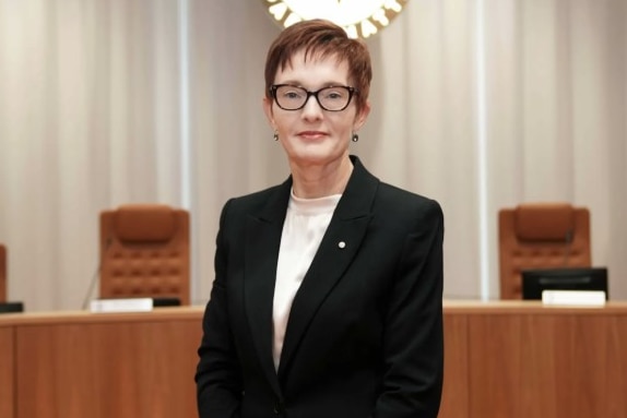 A woman with red hair and glasses wearing a white shirt and black blazer.
