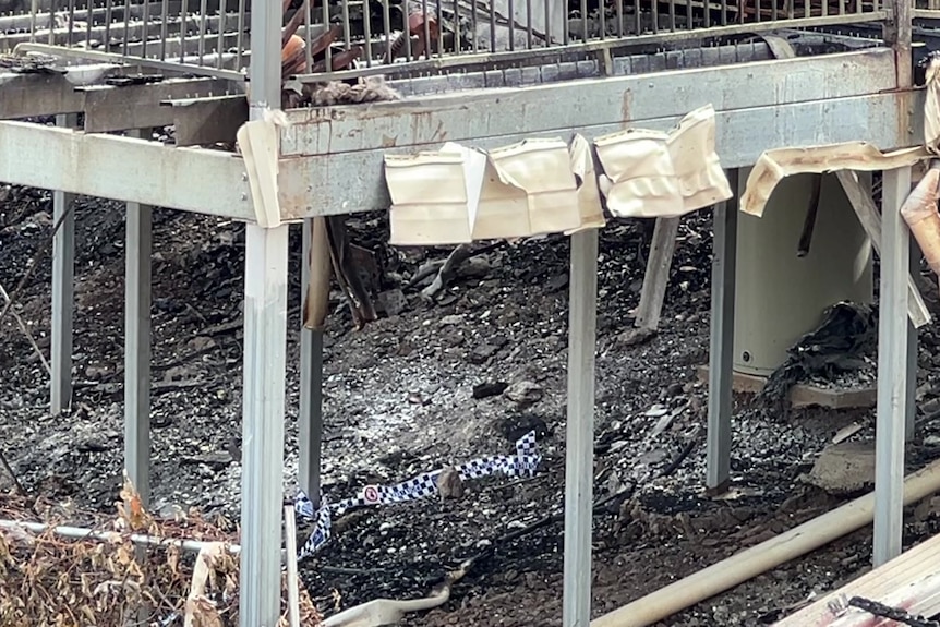 Police tape lying on the ground under a burnt out house