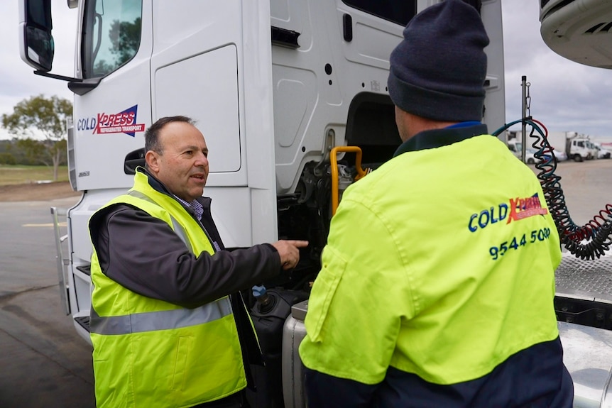 Two men stand talking in front of a truck